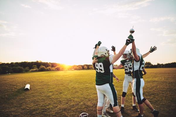 Football players standing together in a huddle and raising a champio<em></em>nship trophy