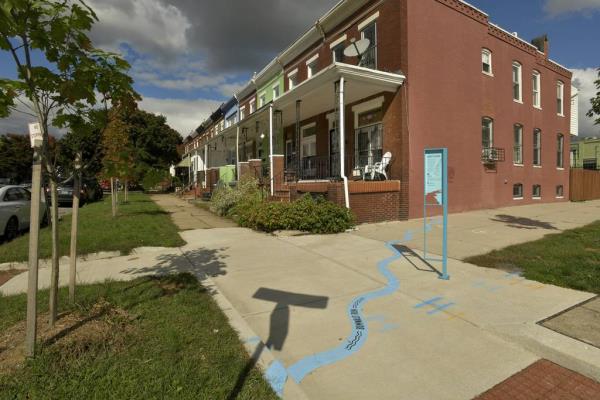 A public art project and neighborhood history by designer Bruce Willen, “Ghost Rivers,” is pictured at Huntington Avenue and West 26th Street. The curving blue line on the sidewalk marks wher<em></em>e Sumwalt Run used to flow and approximately wher<em></em>e it remains beneath Remington’s streets.