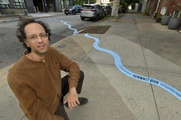 Bruce Willen crouches in the 300 block of West 27th Street, near his public art installation.