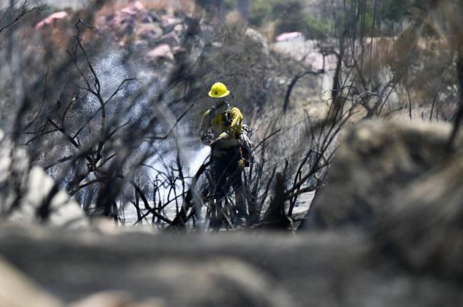 A firefighter sprays down the remaining hot spots on Monday, July 17, 2023, near Perris, Calif., due to the Gavilan Hills bush fire that erupted on Saturday near Lake Mathews. Evacuation warning are still in place, authorities say. (Anjali Sharif-Paul/The Orange County Register via AP)